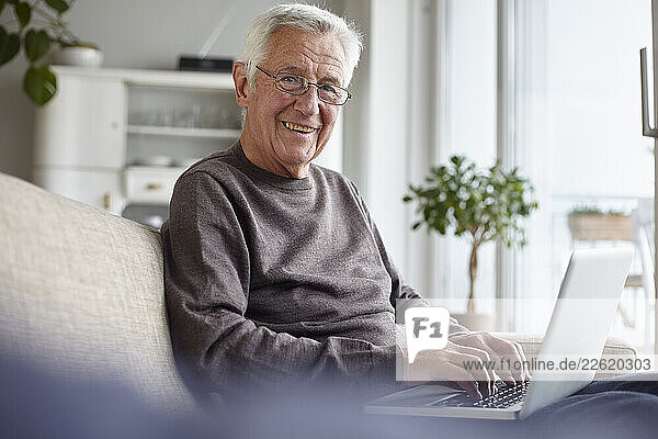 Senior man smiling while using a laptop indoors