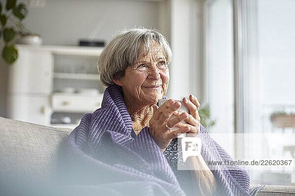 Senior woman enjoying a warm drink at home wrapped in a blanket