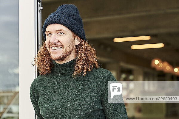 Thoughtful male hipster looking away while leaning on window at studio apartment