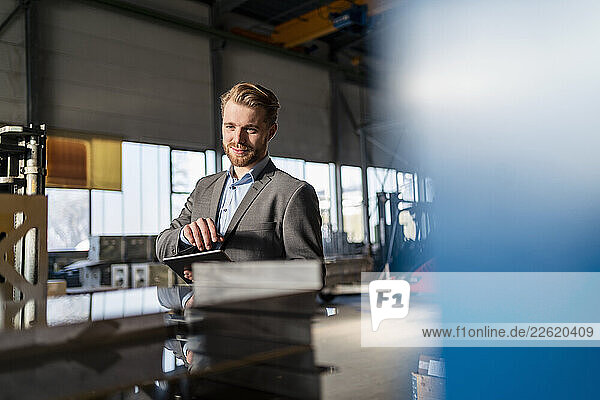 Portrait of a smiling young businessman with tablet in a factory