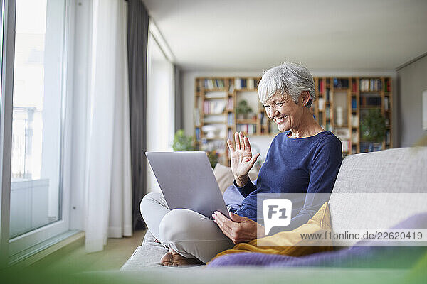 Senior woman at home using laptop for a video call in the living room