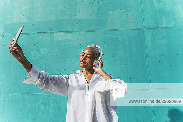 Beautiful woman standing in front of teal wall  listening music  taking selfies