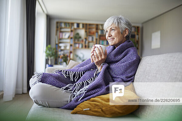 Senior woman relaxing at home with a cup of tea and a blanket