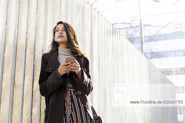 Young woman with smartphone in the city looking around