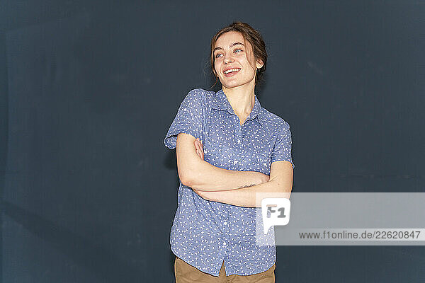 Smiling woman in a blue shirt with arms crossed indoors