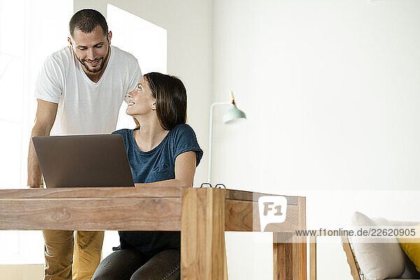 Smiling couple working at laptop from home in home office in modern living room