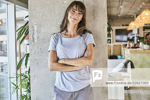 Mature woman standing with arms crossed against wall at home