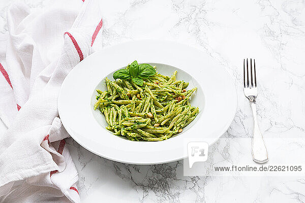 Ligurian trofie pasta with Genoese pesto  basil  and pine nuts on a marble surface with a fork and kitchen towel.