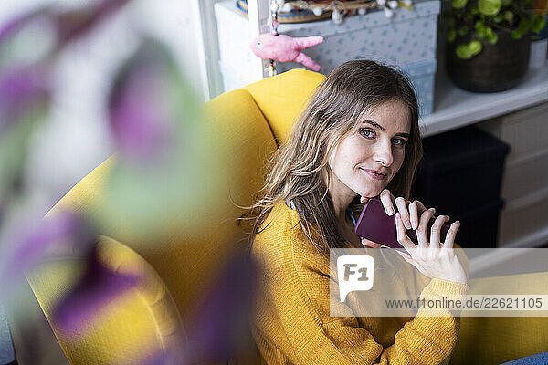 Woman sitting in a yellow armchair at home holding a smartphone