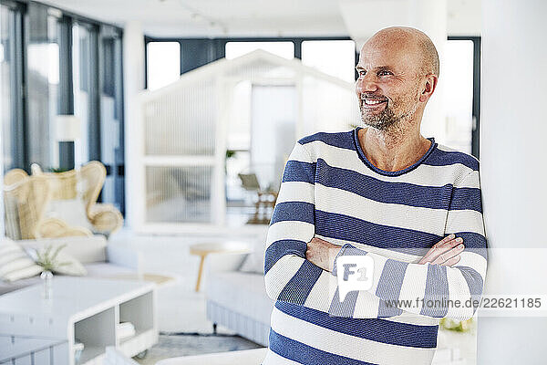 Smiling man with arms crossed looking away while standing at home