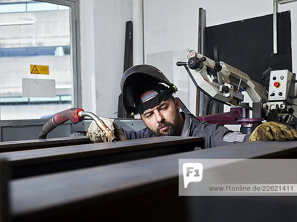 Welding technician inspecting metalwork with protective equipment in his workshop