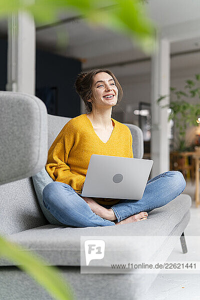 Woman sitting on a sofa with a laptop in a modern loft apartment