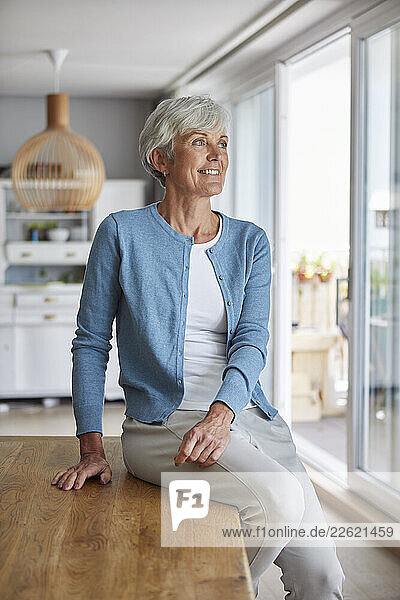 Woman in a blue cardigan smiling while sitting on a wooden table at home