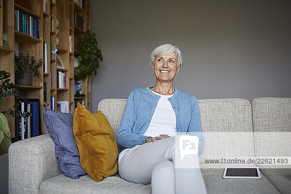 Smiling woman sitting on a sofa at home with a tablet nearby