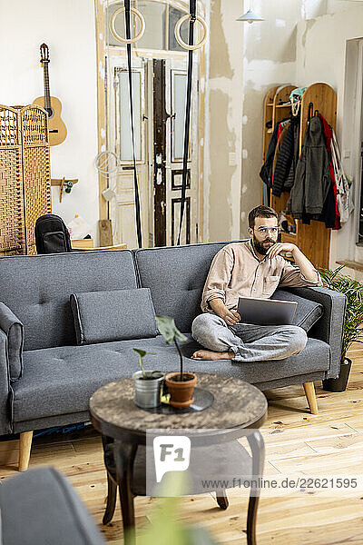 Young man sitting at home on couch  using digital tablet