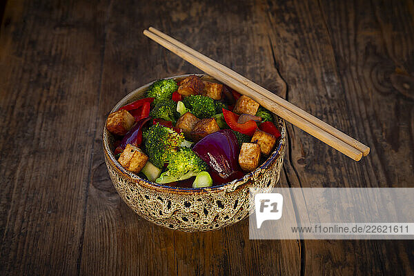 Vegan bowl with broccoli  red onion  peppers  and tofu on a wooden table
