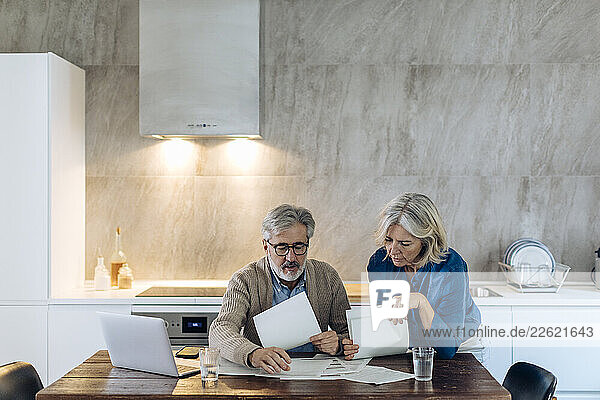 Mature couple with papers and laptop on kitchen table at home