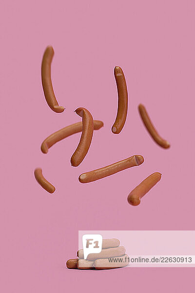 Bavarian sausages falling midair on pink background