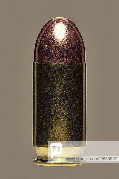 Close up studio shot of shiny .45 bullet on brown background
