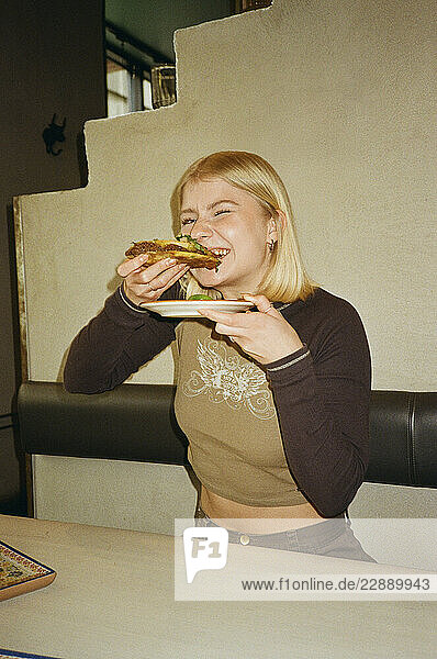 Smiling young woman with blond hair eating tacos at fast food restaurant