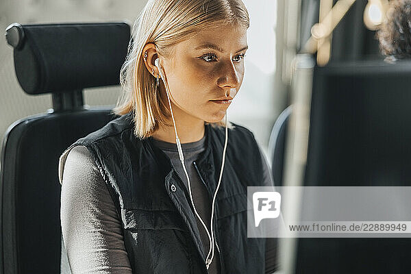 Focused young female entrepreneur wearing headphones working on computer in tech office