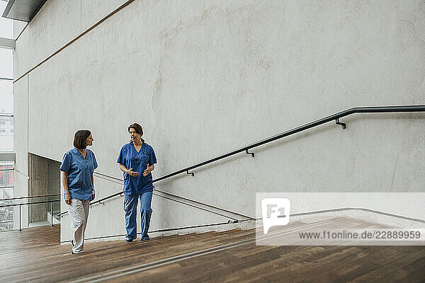 Full length of female doctors wearing medical scrub moving up on stairs in hospital building