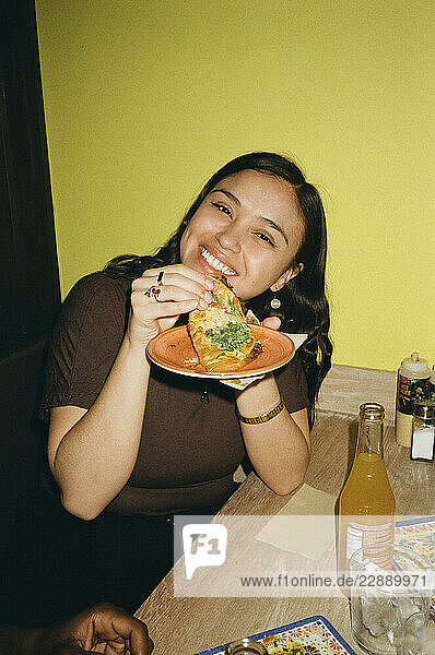 Portrait of smiling young woman eating tacos at fast food restaurant