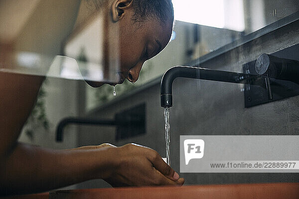 Low angle view of woman washing face with faucet water in bathroom
