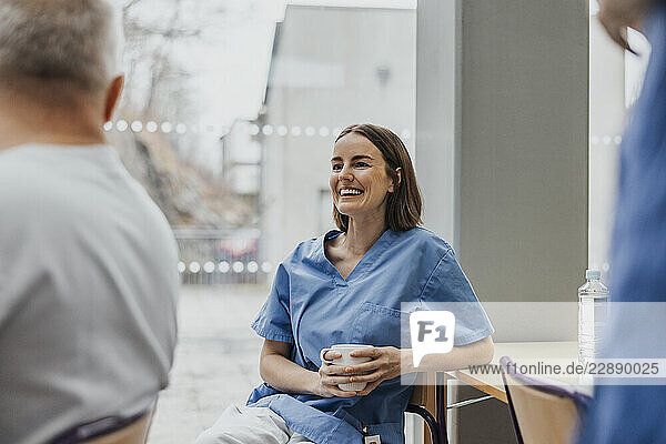 Happy female healthcare worker sitting with coffee mug in hospital cafeteria