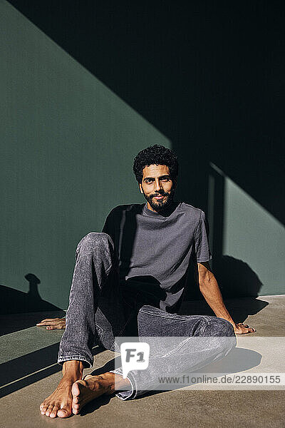 Smiling man sitting on floor near wall at home
