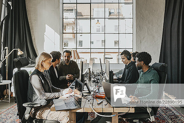 Group of multiracial computer professionals working on desktop PC while sitting at desk in tech startup office