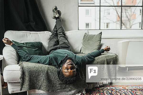Carefree businessman listening to music while lying on sofa with feet up in office