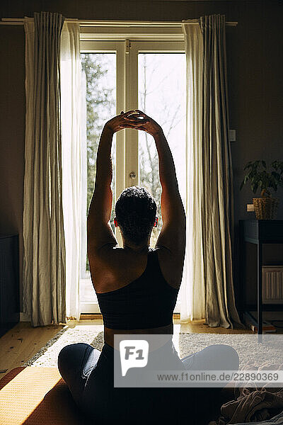 Rear view of woman doing stretching exercise while sitting at home