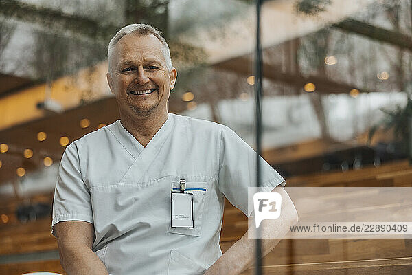 Portrait of smiling mature male healthcare worker wearing medical scrub seen through glass