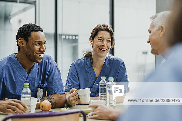 Happy male and female medical professionals enjoying breakfast in cafeteria at clinic