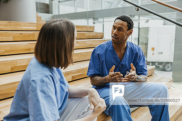 Male doctor discussing with female nurse while sitting on steps in hospital building