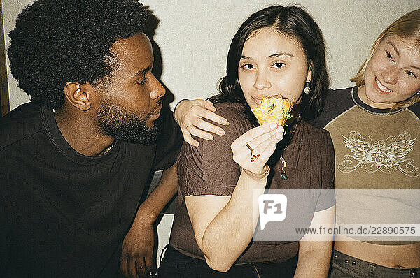 Portrait of woman holding piece of taco while sitting with friends at restaurant