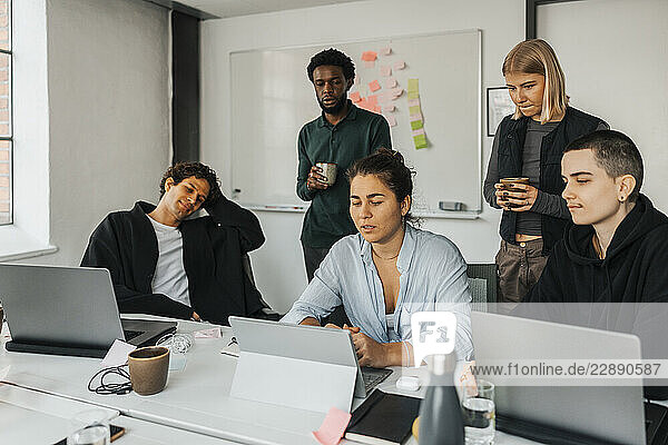 Young businesswoman explaining ideas to colleagues through laptop while working in startup office