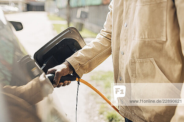 Midsection of mature man charging electric car with plug at street