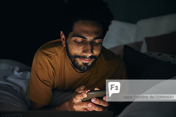 Smiling man using smart phone in bedroom at night