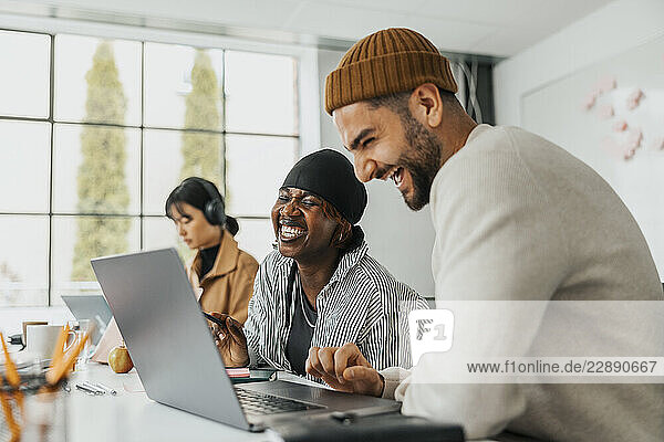 Happy male and female business professionals laughing while working together at office