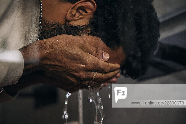 Man washing face with water in bathroom