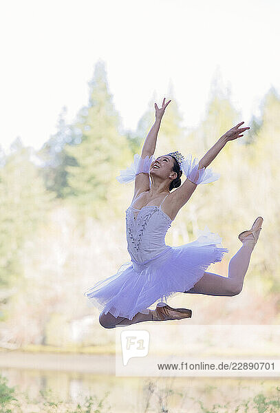 Ballet dancer in mid-air leap against a blurred forest background. WA  USA