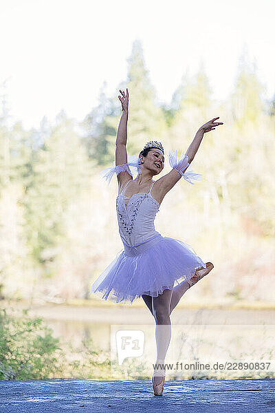 Ballerina in a white tutu dancing gracefully outdoors against a forest backdrop. WA  USA