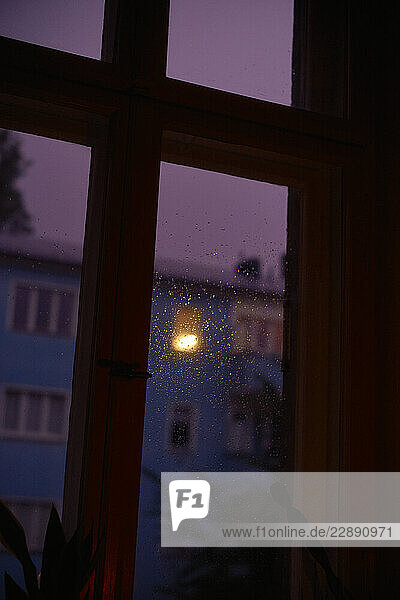 Rain-speckled window with a view of a blue building at dusk.