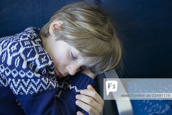 Young child sleeping on an airplane seat wearing a patterned blue sweater. Sicily  Italy
