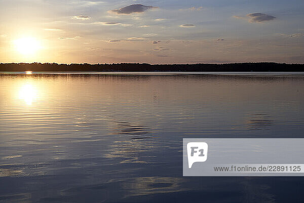 Sunset over a tranquil lake with calm water reflecting the evening sky. Mecklenburg Lake Plateau  Mecklenburg-Western Pomerania  Germany