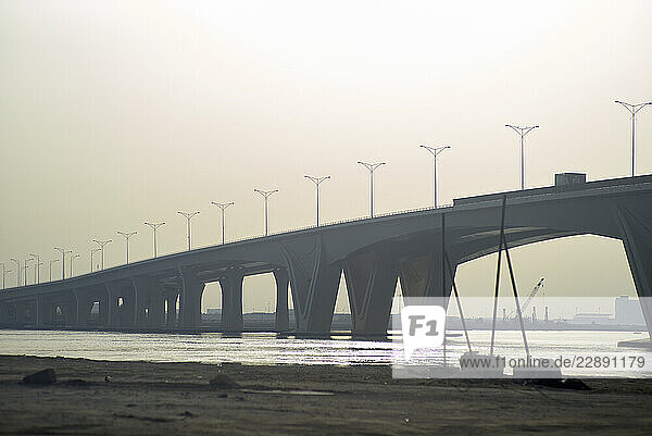 A long concrete bridge stretches across a calm river under a hazy sky. Abu Dhabi  UAE