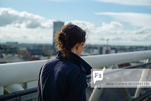 Woman in blue coat with sunglasses looks at cityscape from bridge on a sunny day. Brussels  Belgium