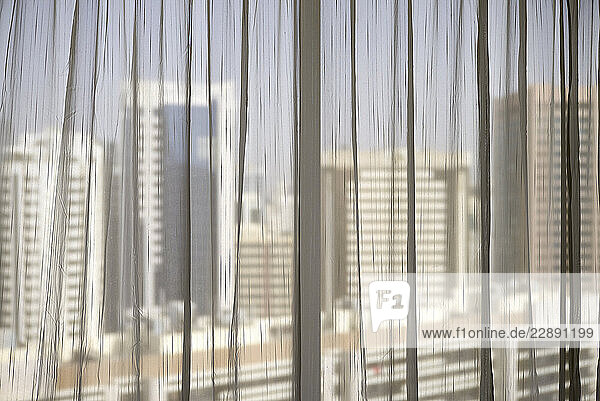 Tall city buildings viewed through sheer curtains from indoors. Abu Dhabi  UAE